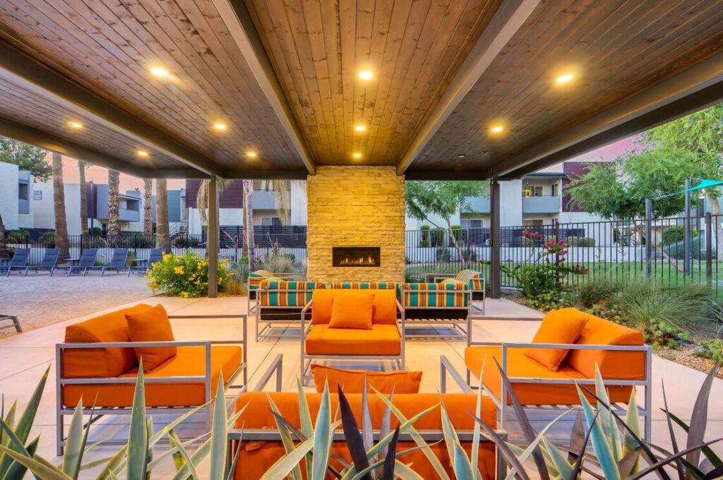 A covered pavilion with bright orange and blue lounge chairs and a fireplace at Scottsdale Gateway apartments in North Tempe, AZ