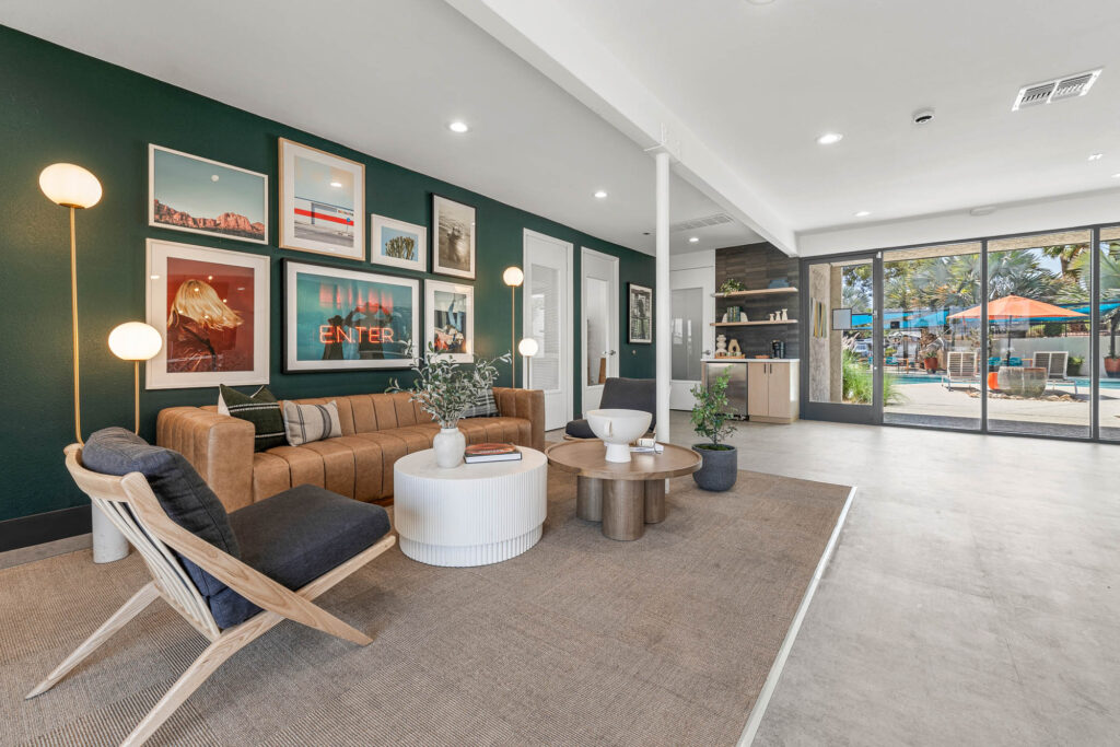Leasing office lounge area with sofa, chairs and green accent wall with framed art on it. A large window offers a view of the patio and pool