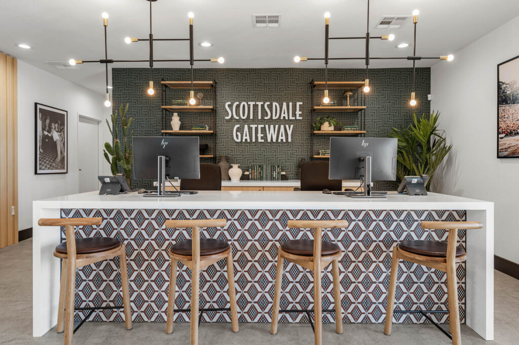Leasing off reception area with a patterned desk, four wooden chairs, two computers, and overhead lighting. "Scottsdale Gateway" sign on a textured wall behind desks.