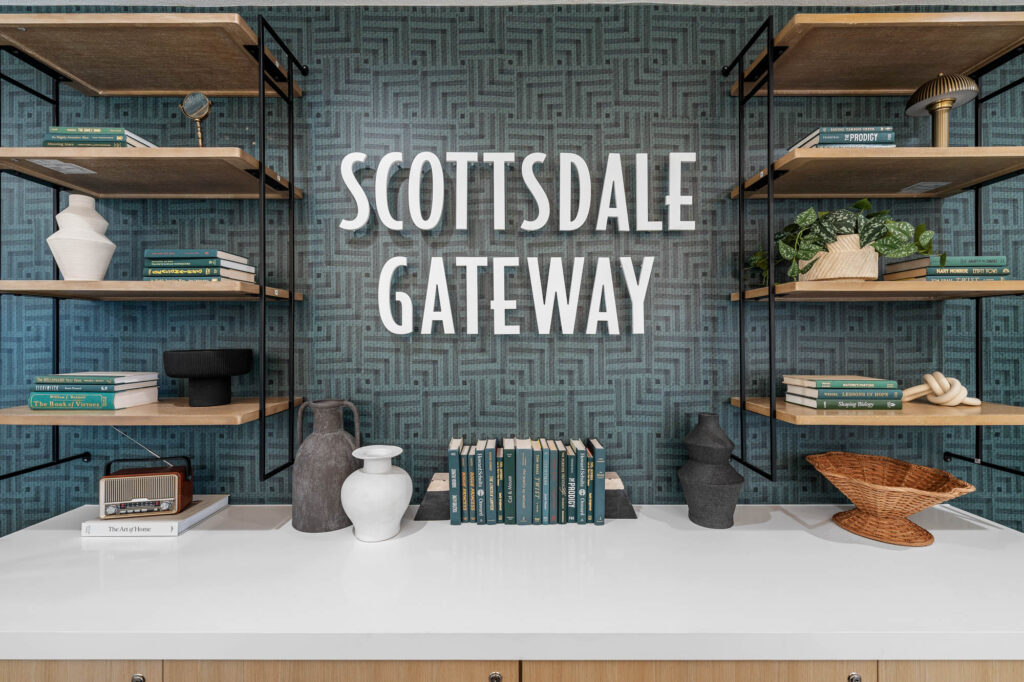 Blue geometric wall with "Scottsdale Gateway" text it and wooden shelves with books, vases, and decorative items on them.